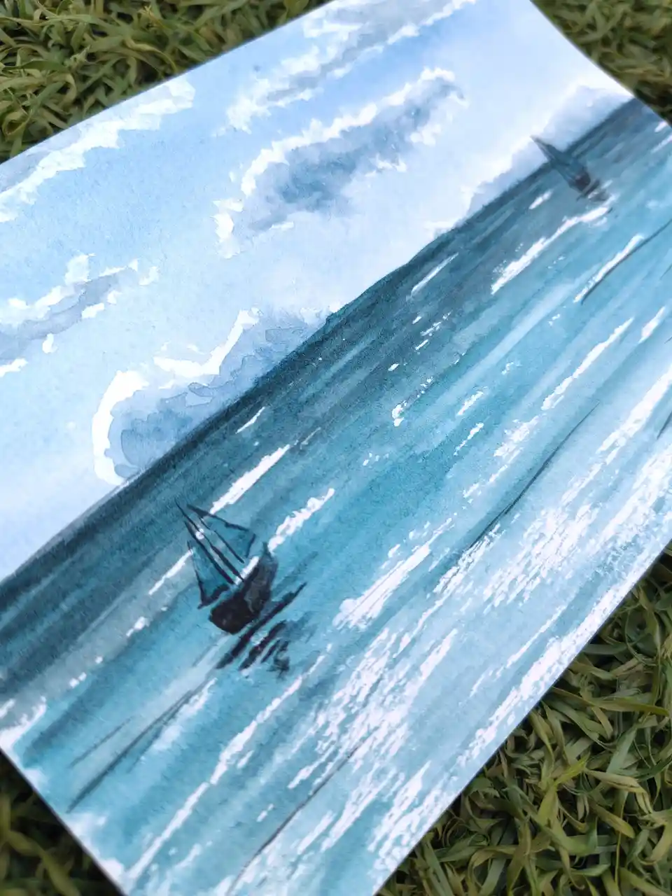 A watercolor painting of two sailboats on a blue sea under a cloudy sky, lying on green grass. The overlaid text reads 'i'm…