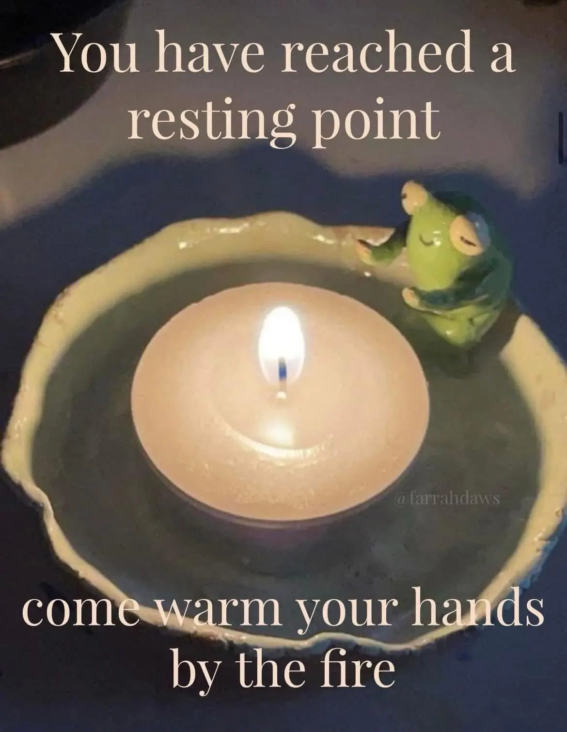 A lit tea light candle sits in a ceramic holder, with a small green frog figurine resting beside it. The image has text…