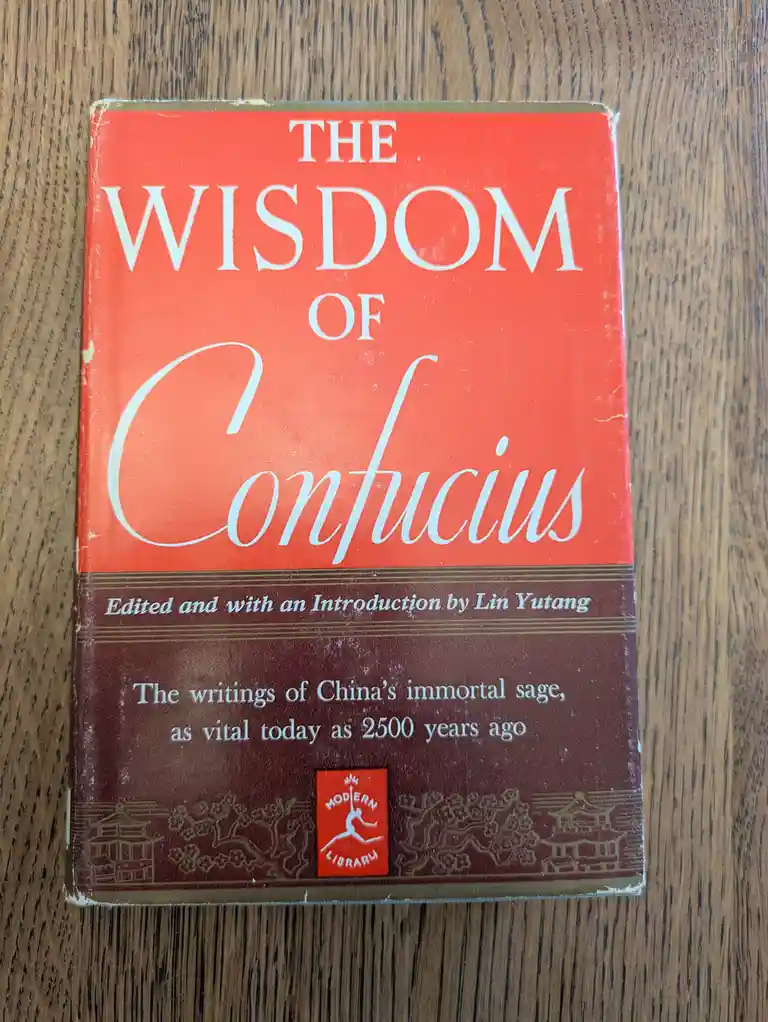 A close-up photo of a well-worn red and brown book titled 'The Wisdom of Confucius', edited by Lin Yutang, resting on a…