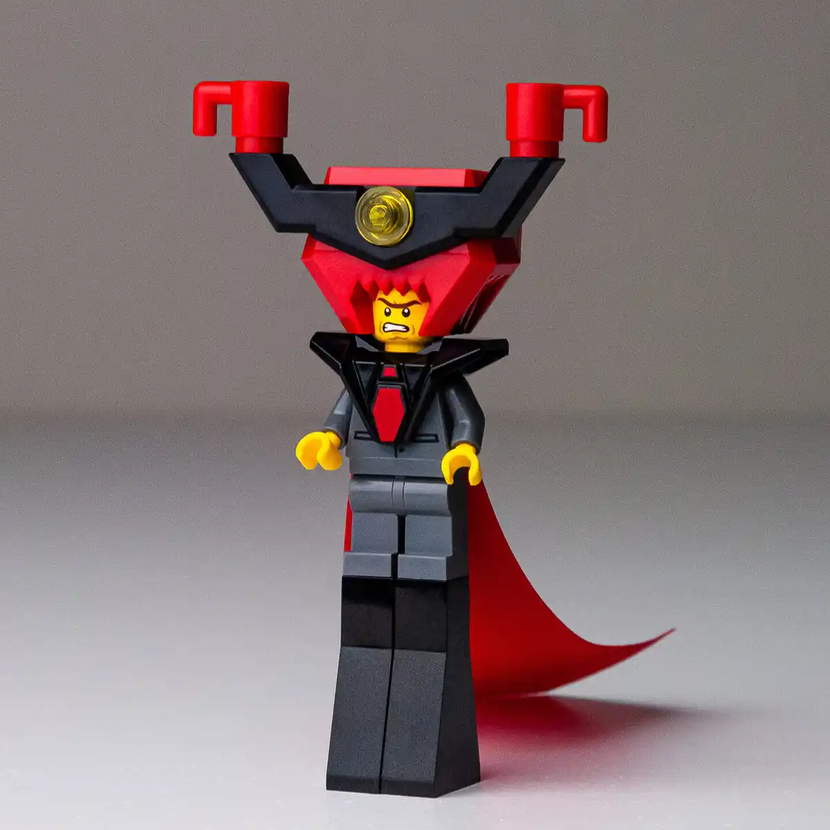 A LEGO minifigure dressed as a villain with a red and black helmet featuring horn-like protrusions, a red cape, and an angry…