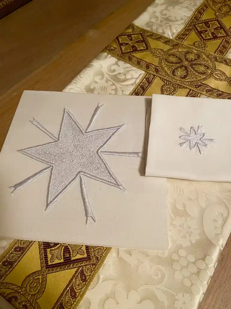 Two white cloth squares with embroidered stars, one large and one small, rest on ornate golden and cream religious…