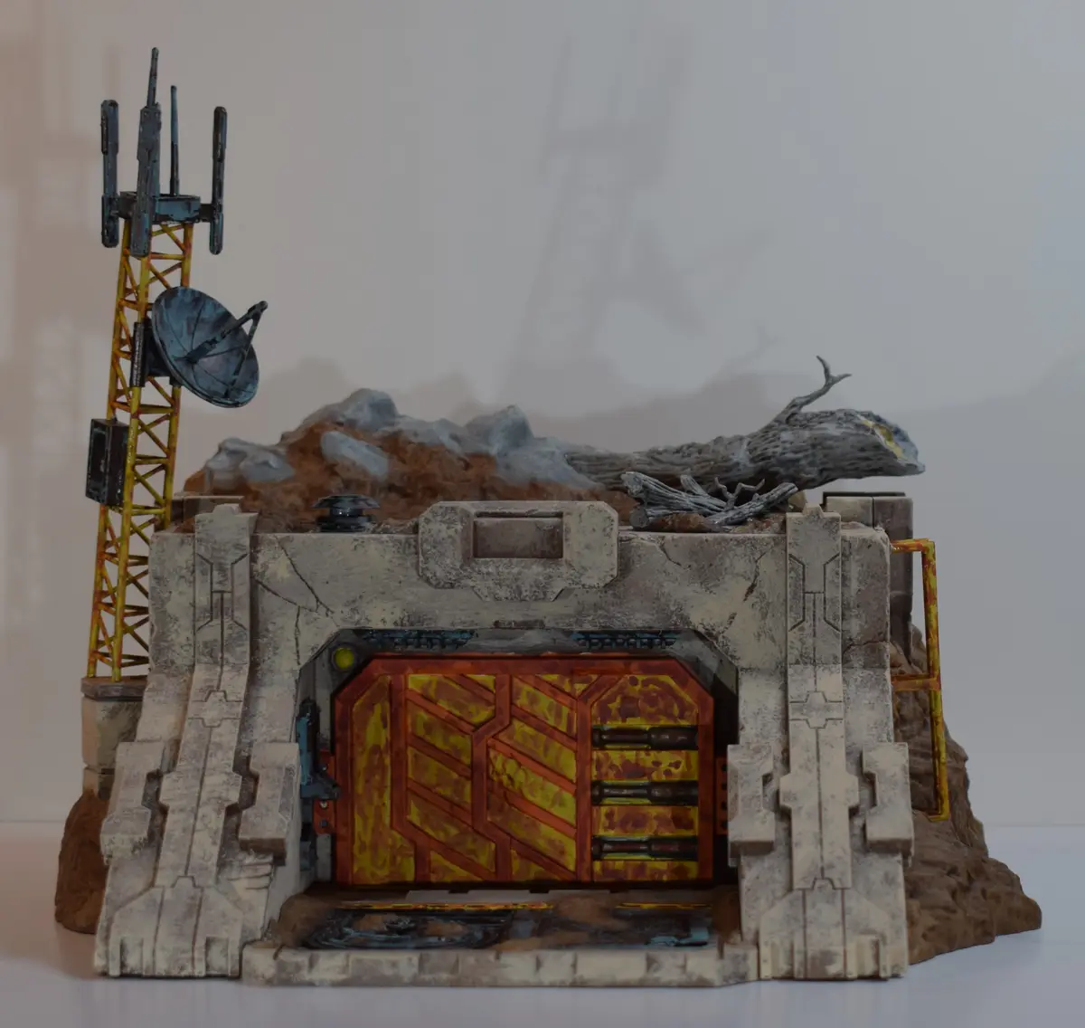 A detailed miniature diorama depicts a weathered, sci-fi style bunker with a rusted orange and yellow door, set against a…