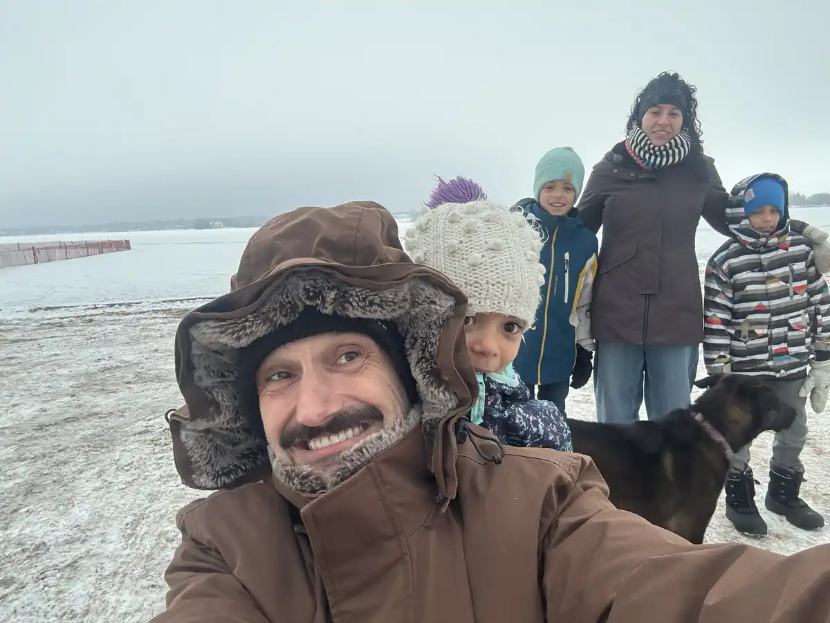 A selfie of a man in a brown winter coat with a fur-lined hood, smiling broadly while holding a child in a white knit hat…