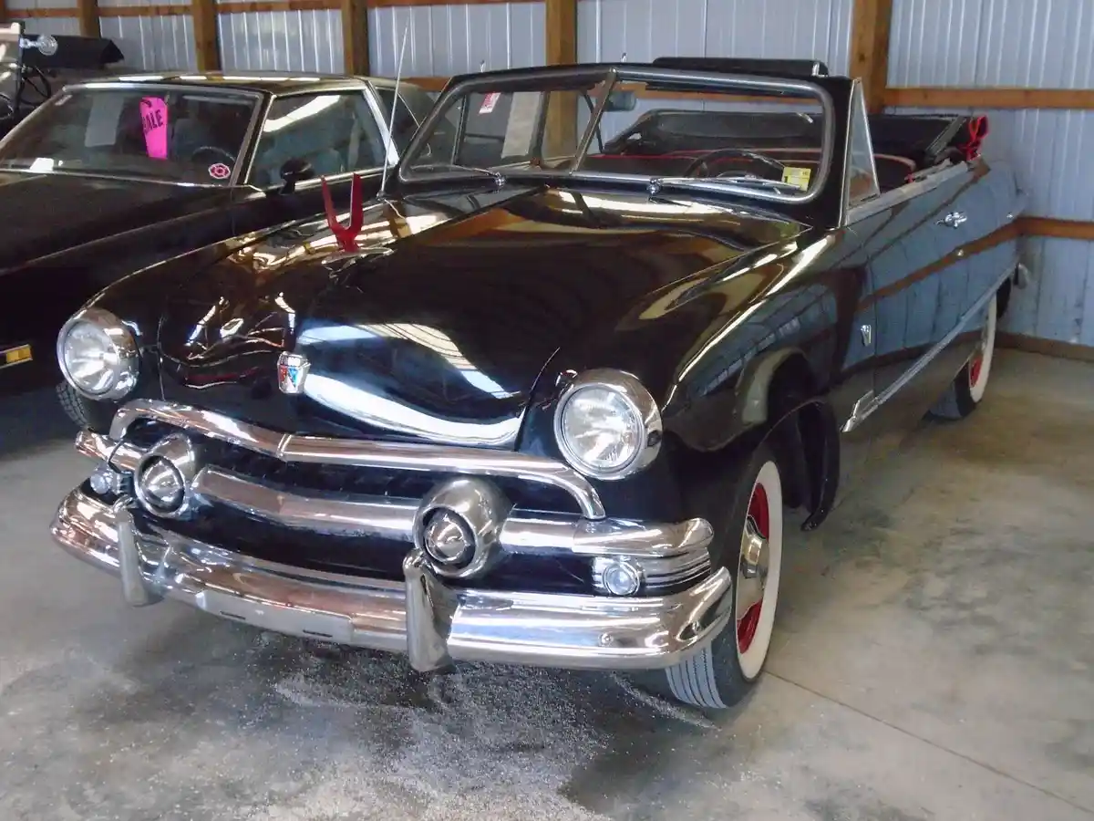 A shiny black vintage convertible car with chrome details and red accents is parked inside a garage. The car has a prominent…