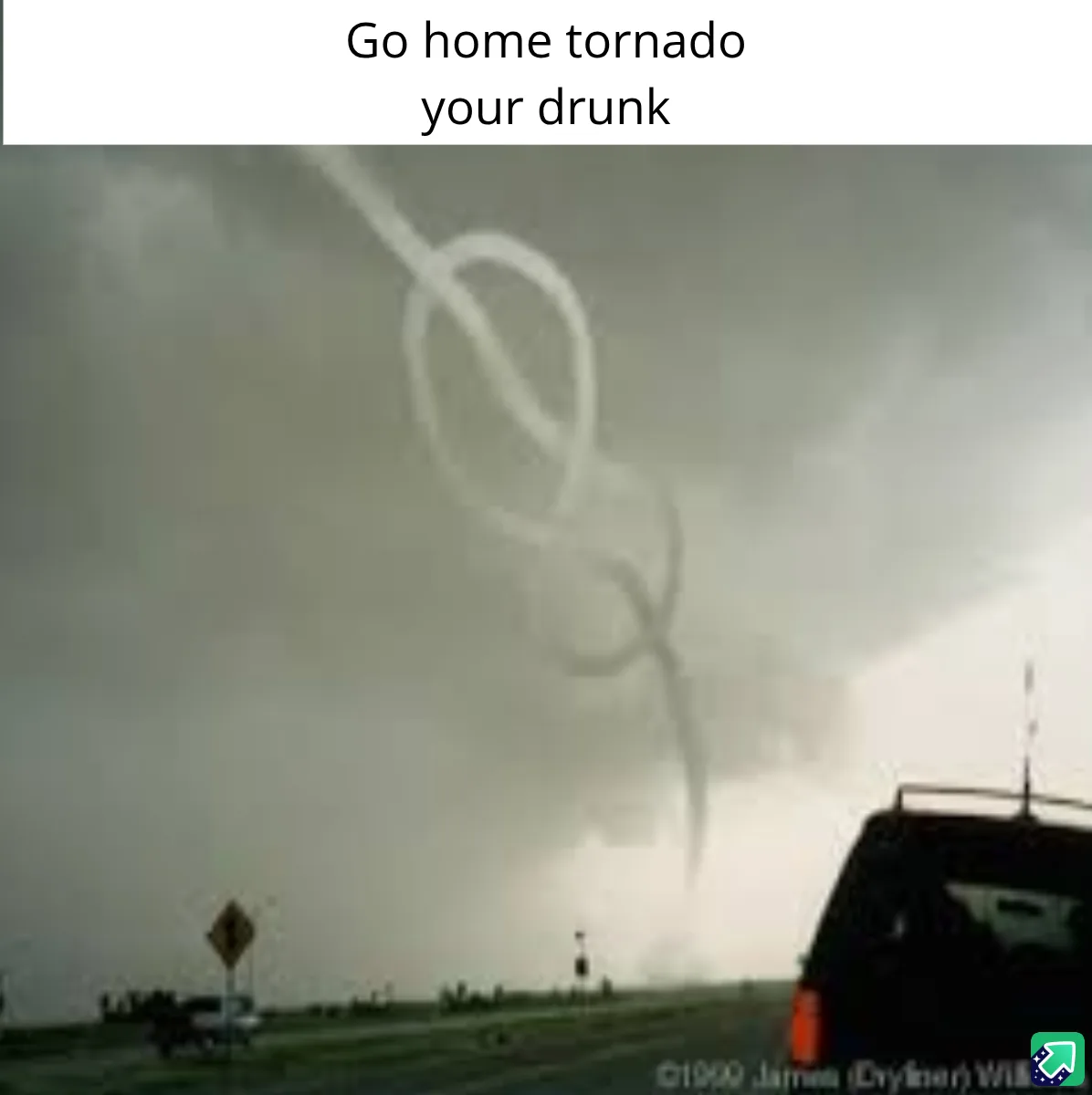 A photograph shows a tornado with a distinct knot-like shape in the sky, viewed from inside a vehicle on a road. The…