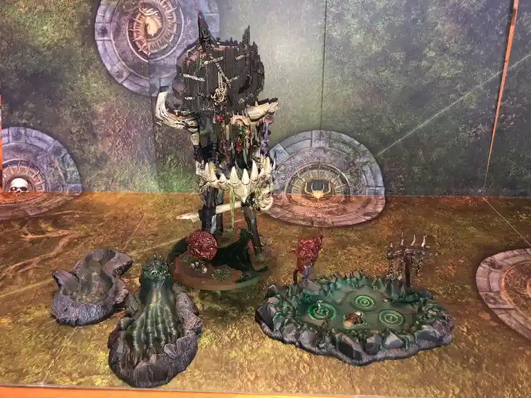 A highly detailed, grimdark fantasy miniature of a towering, skeletal, and monstrous figure stands on a circular base…