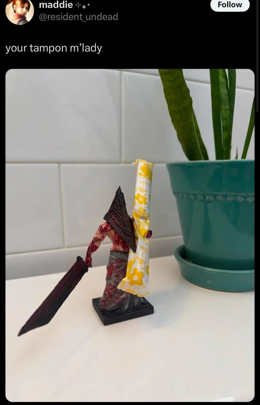 A figurine of the video game character Pyramid Head from Silent Hill, standing on a white countertop, is holding a tampon in…