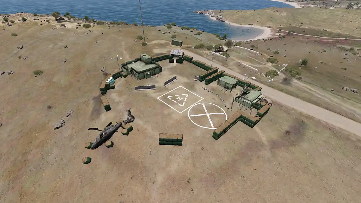 An aerial view of a military-style compound with green sandbag walls, a helicopter wrecked outside, and two landing zones…
