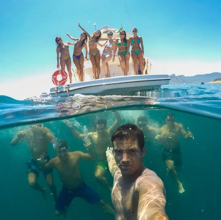 A split-level photo shows a group of women in bikinis posing cheerfully on a yacht above water, while below the surface, a…