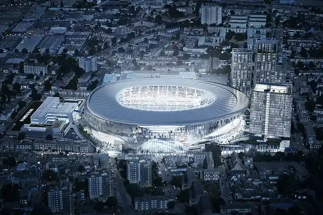 an aerial night view of a large, modern, circular stadium illuminated in a cityscape, with the text 'this is the new stadium…
