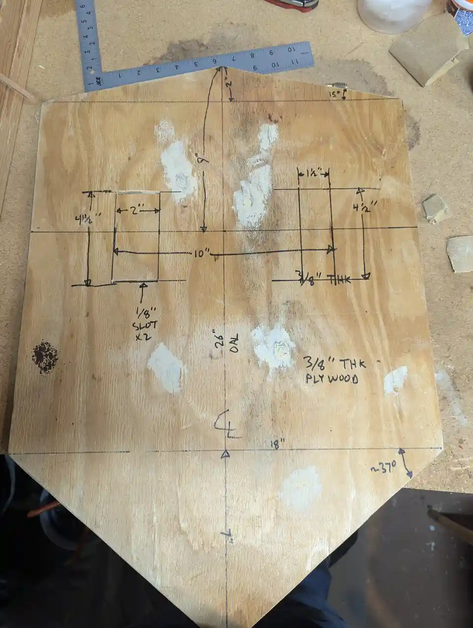 A piece of 3/8" thick plywood is laid out on a workbench with detailed hand-drawn measurements and markings, including…