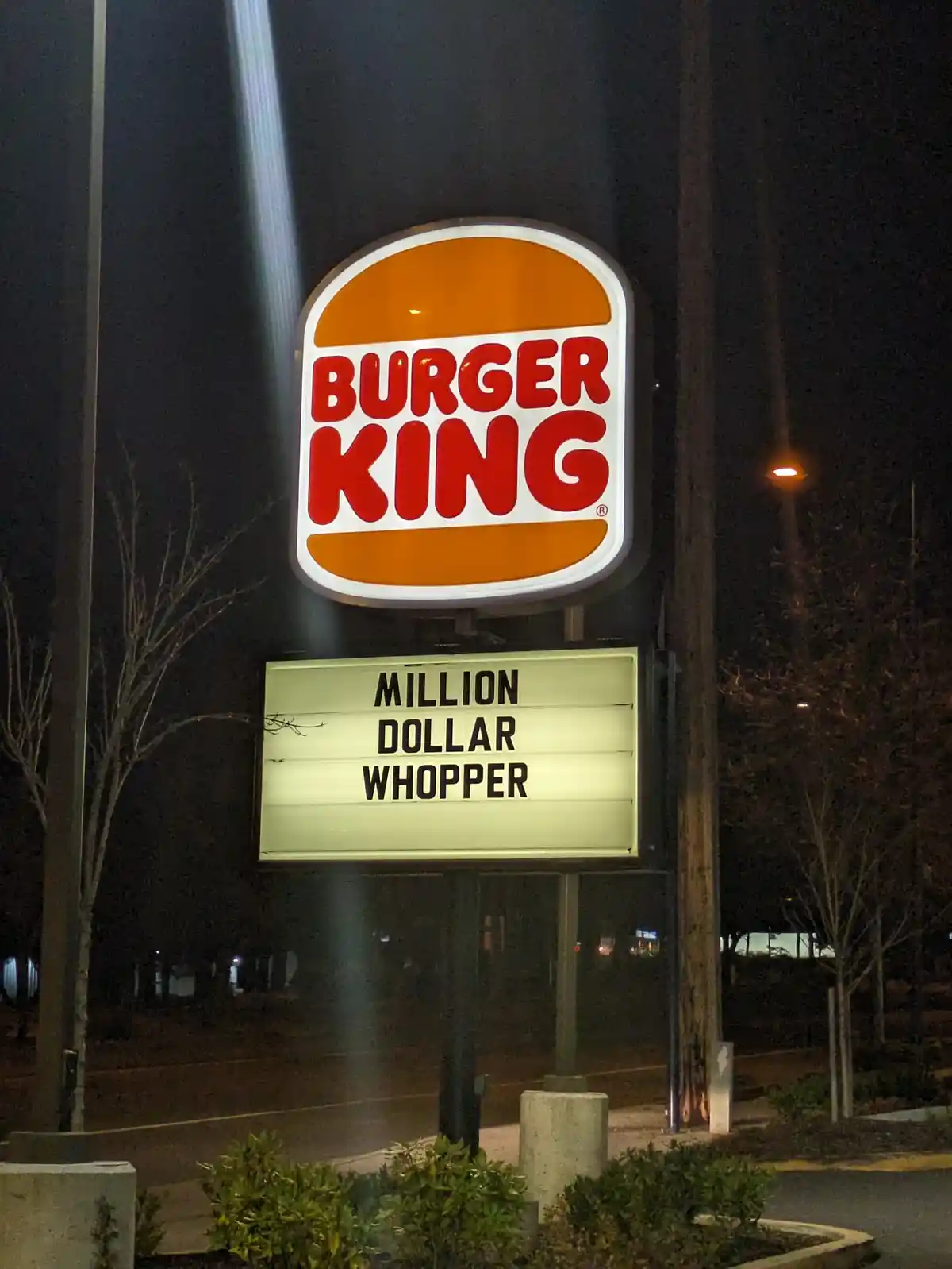 A nighttime photo of a Burger King restaurant sign, featuring the iconic orange and red logo above a lit marquee board that…