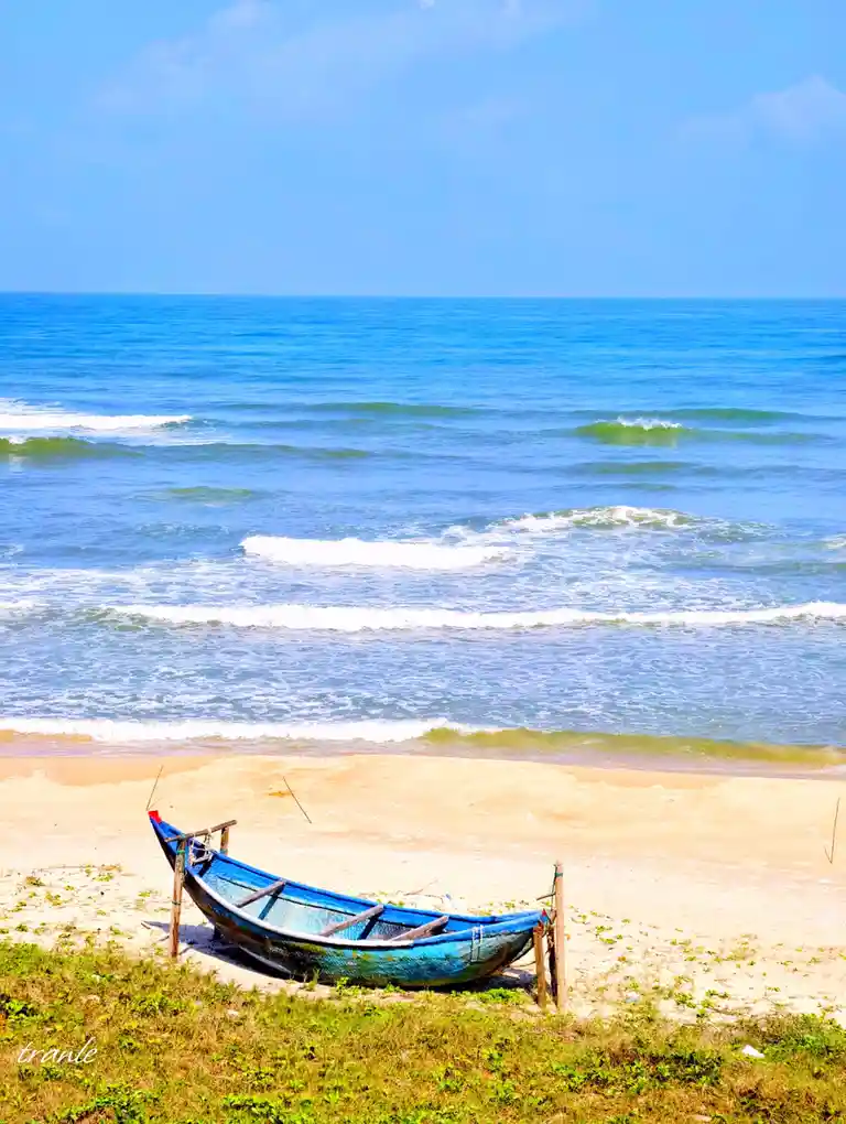 A weathered blue wooden boat rests on a sandy beach, propped up by wooden posts near the water's edge. The ocean stretches…