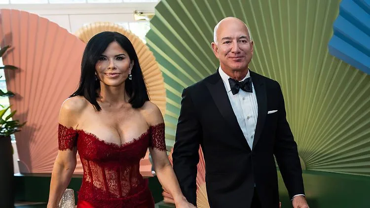 A photo of Jeff Bezos and his wife MacKenzie Bezos at a formal event, with Jeff in a black tuxedo and MacKenzie in a red…