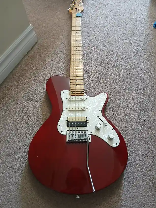 A red electric guitar with a white pickguard lies on a beige carpet, its chrome hardware and pickups visible. The overlaid…