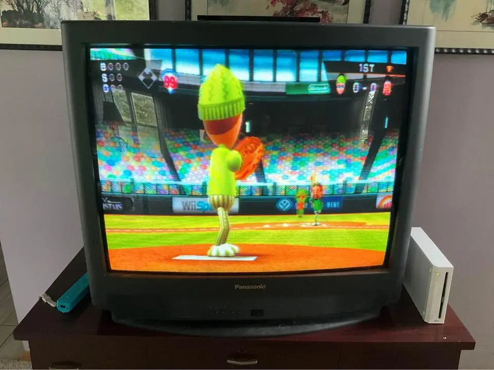 A photo of a Panasonic CRT television displaying a baseball video game, likely 'Wii Sports', featuring a green, carrot-like…