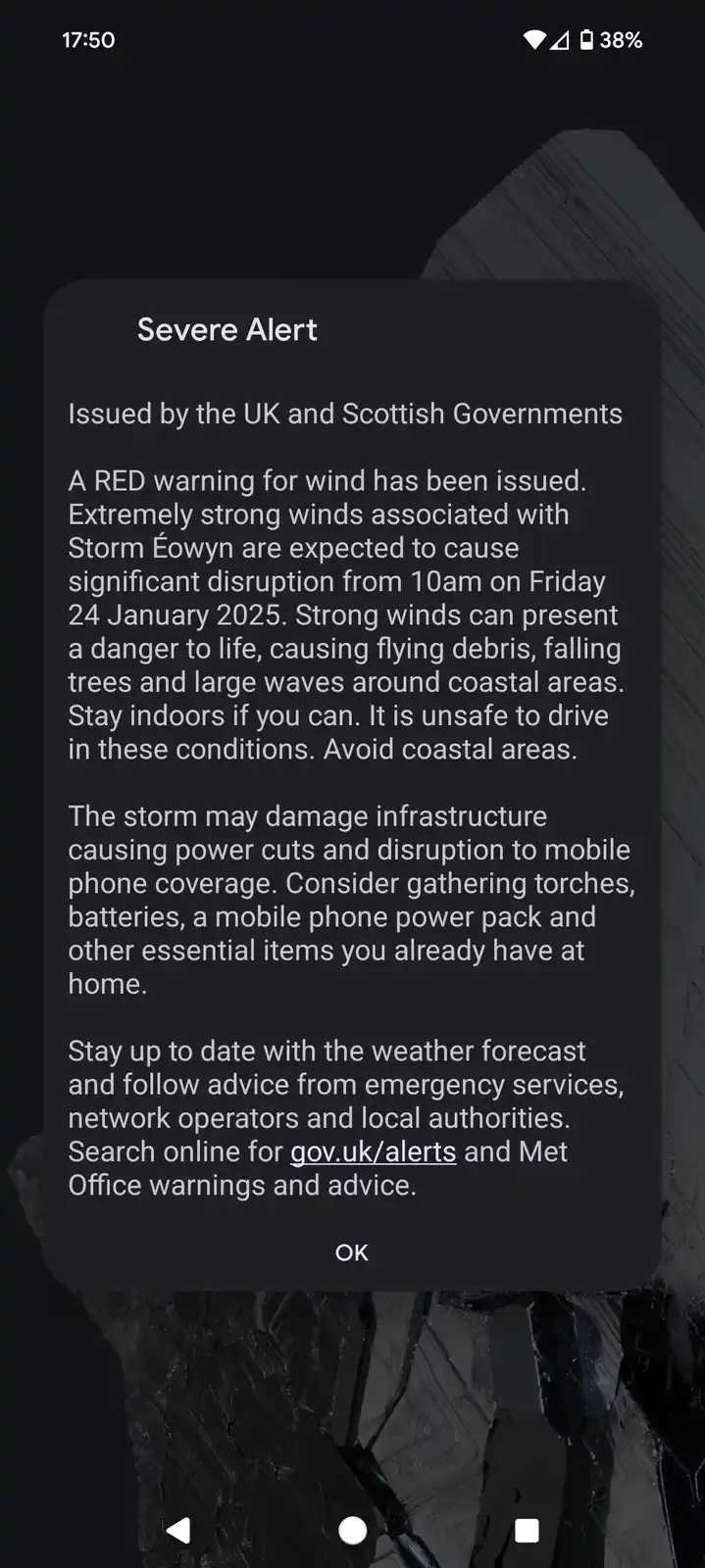 A smartphone screen displays a 'Severe Alert' notification from the UK and Scottish Governments, warning of a red wind…