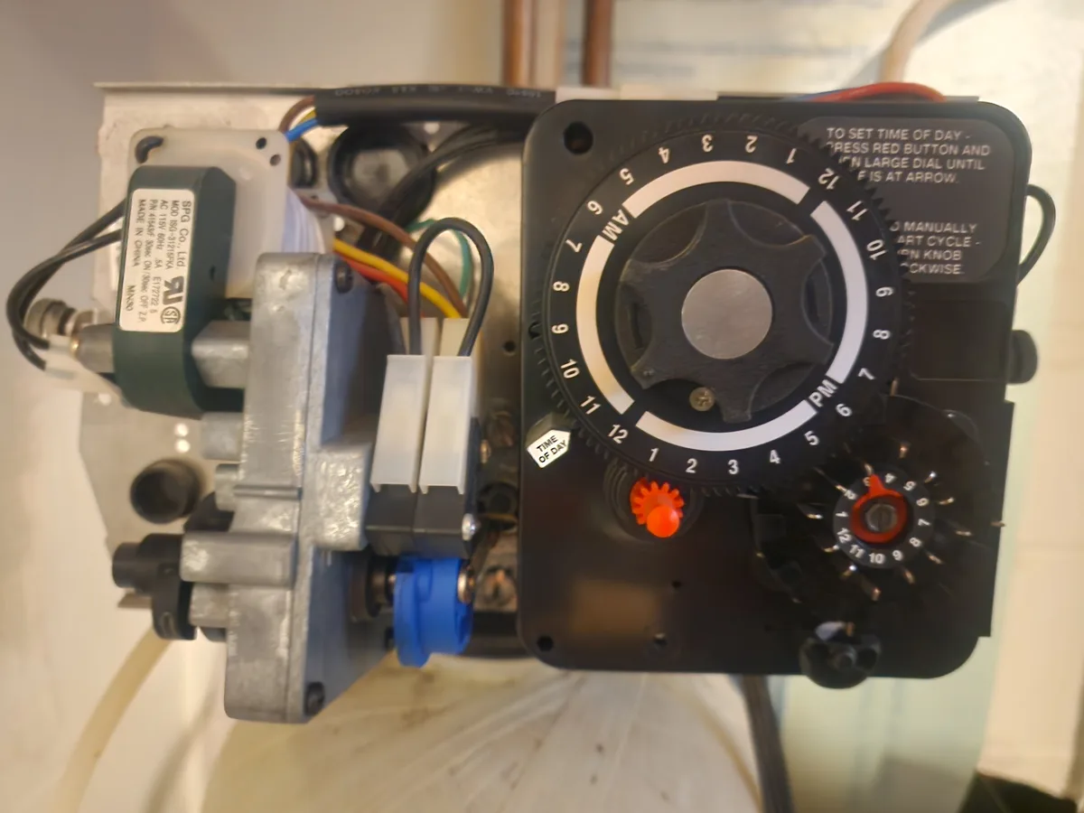 A close-up photo of a mechanical time switch with a large dial marked 1-12 for AM/PM and a small red knob. The device has…