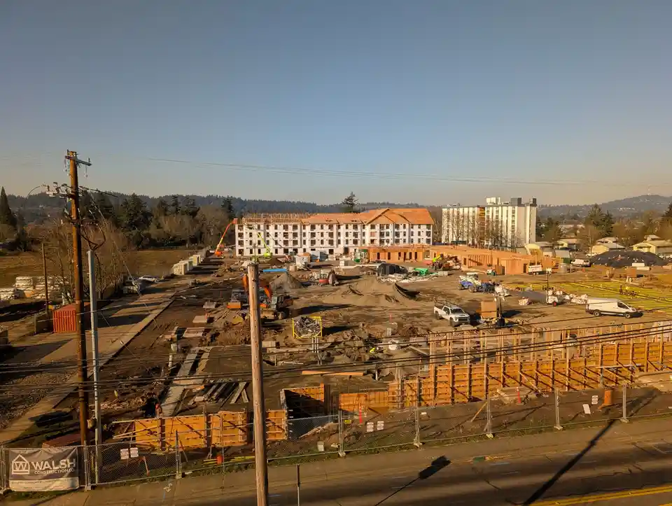 A wide-angle photo of a large, active construction site under a clear blue sky, featuring partially built multi-story…