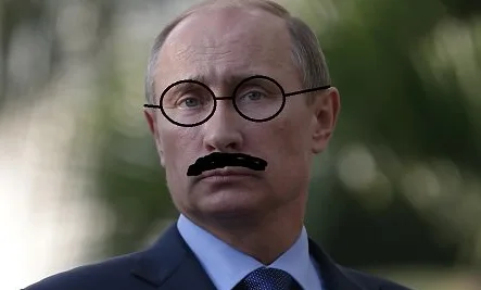 a close-up photo of Vladimir Putin with digitally added round glasses and a thick black mustache, overlaid with the text…