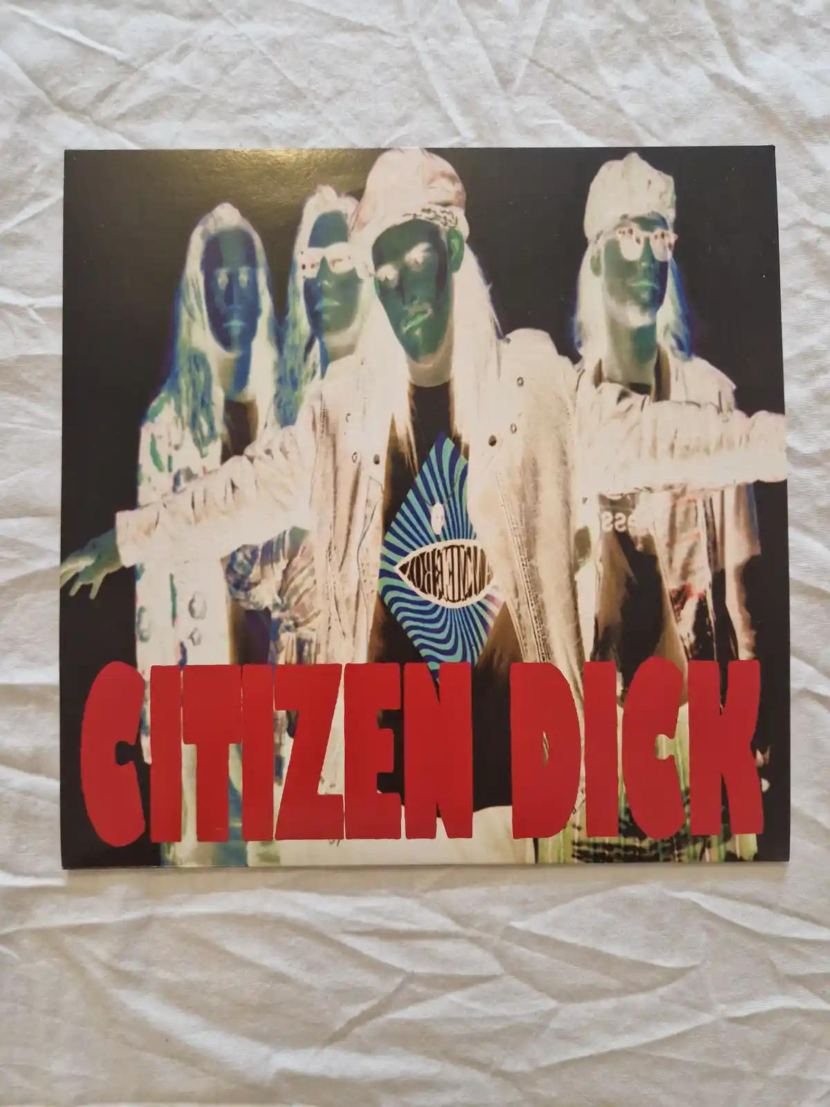A photo of four people with green faces and white clothing, posing with arms outstretched, overlaid with large red text…
