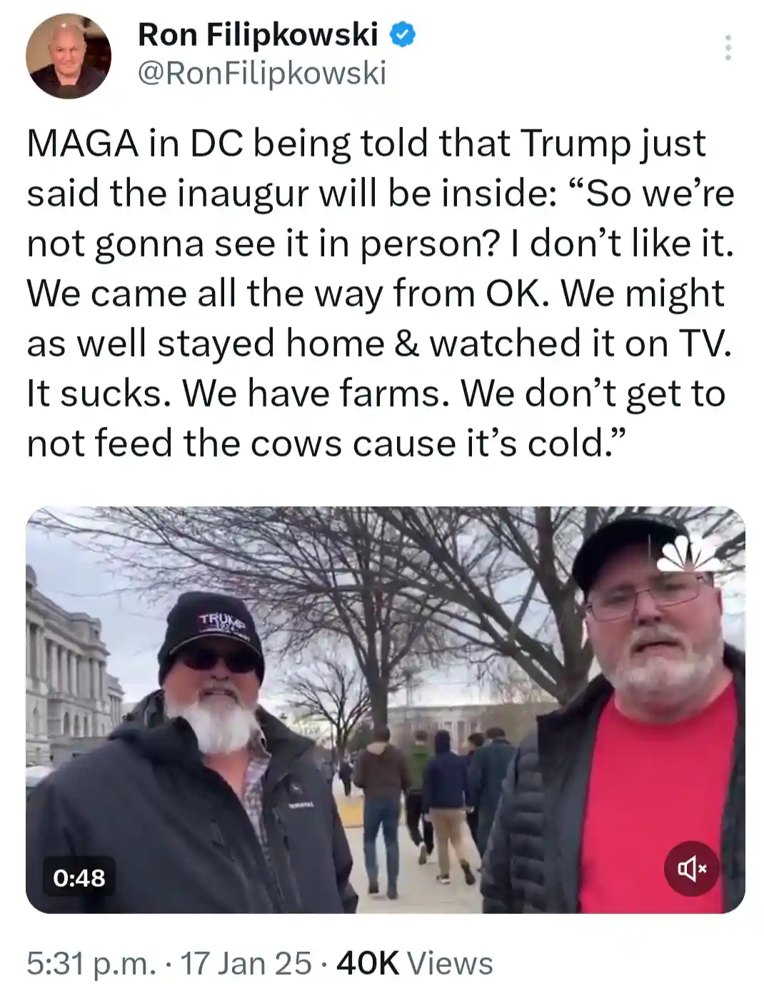 Two men stand outdoors in a city setting, one wearing a 'TRUMP' beanie and sunglasses, the other in a red shirt and cap. The…