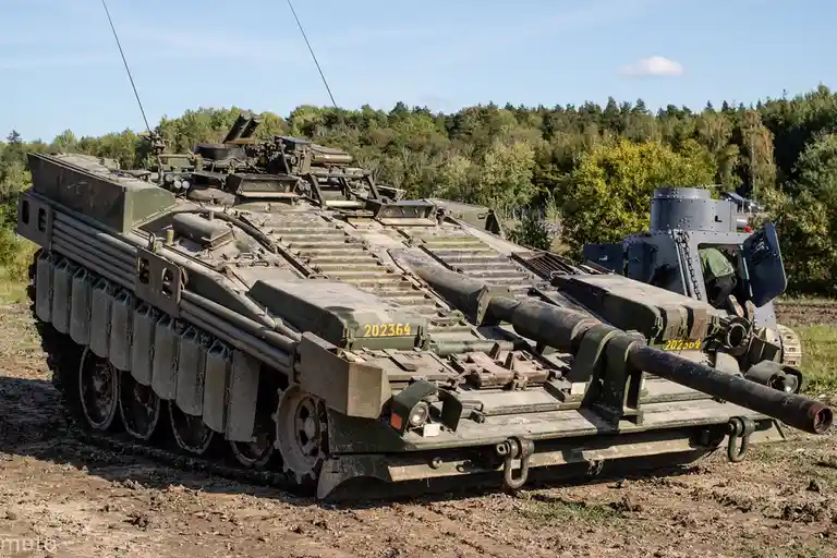 A military tank with a second, smaller tank mounted on its turret, both bearing the number 202364. The overlaid text reads…