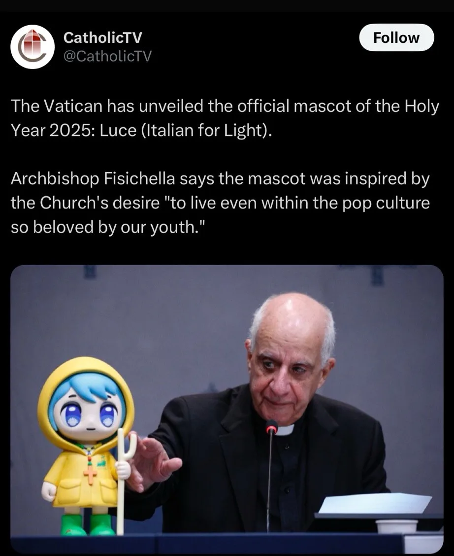 An older man in clerical attire sits at a podium, gesturing toward a small, yellow, anime-style mascot figure with blue hair…