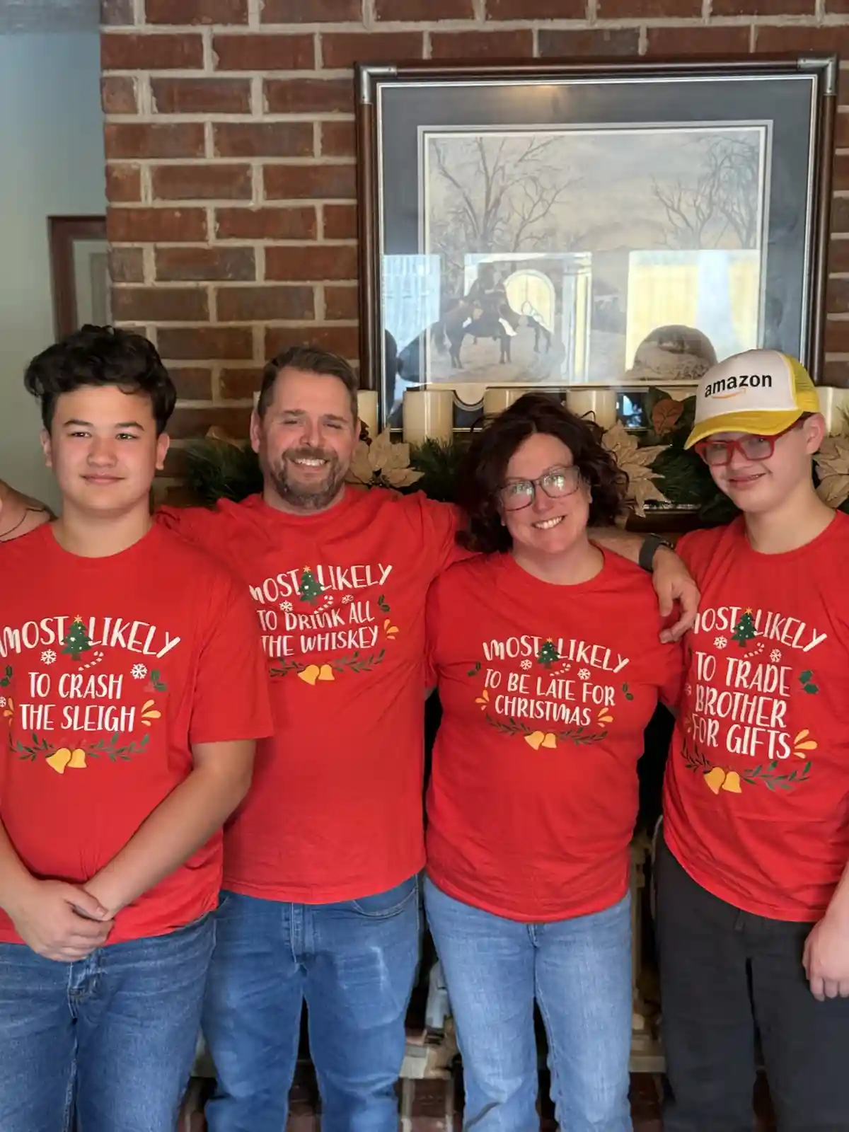 Four people pose together in front of a brick fireplace wearing matching red Christmas-themed t-shirts with humorous 'most…