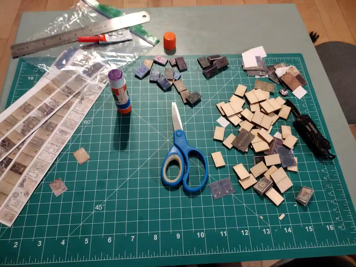 A green cutting mat is covered with craft supplies including blue scissors, glue sticks, rulers, and a multi-tool. Scattered…
