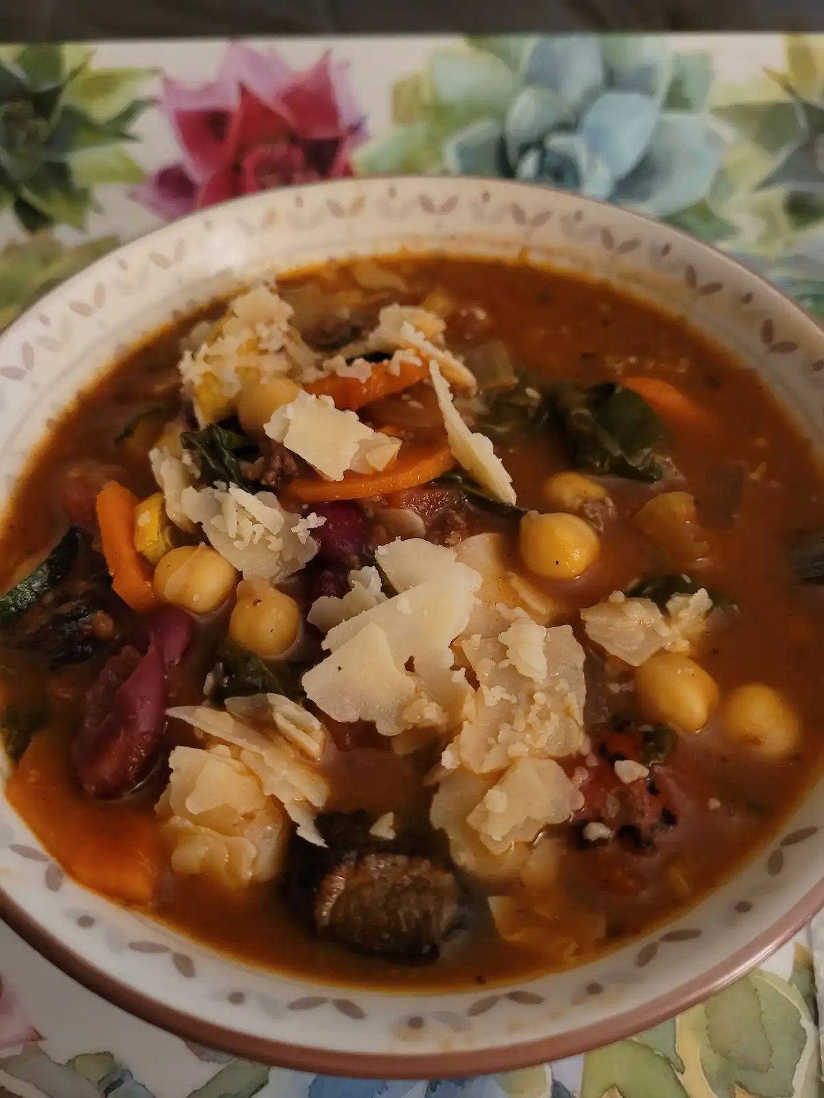 A close-up photo shows a bowl of hearty, reddish-brown vegetable and bean soup with visible chickpeas, carrots, kidney…