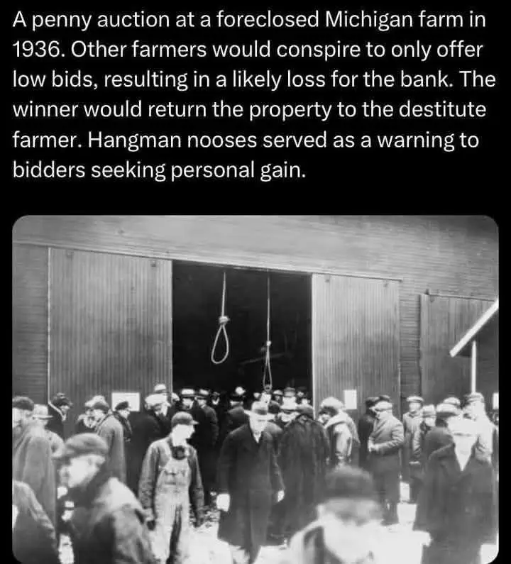 A black-and-white historical photo shows a crowd of men in 1930s attire gathered outside a barn. Two nooses hang prominently…