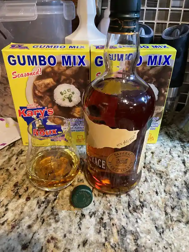 A bottle of Sazerac bourbon whiskey and a glass of poured liquor sit on a granite countertop, flanked by two yellow boxes of…