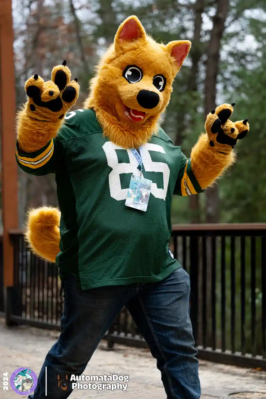 A person in a yellow wolf mascot costume wearing a green football jersey with the number 85 and a staff ID badge that reads…