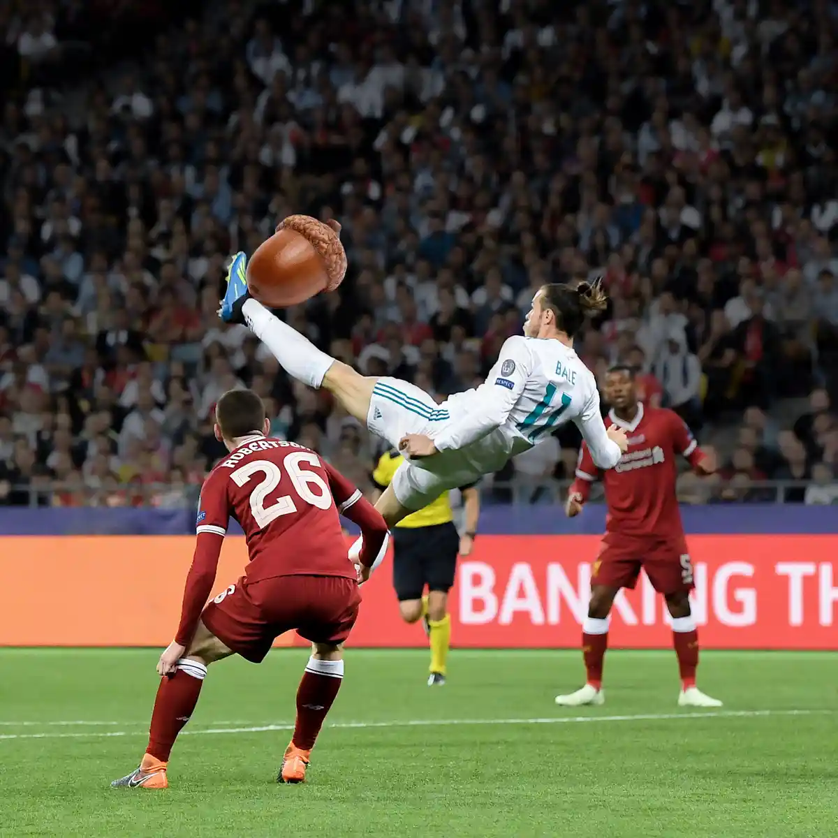 A soccer player in a white jersey with 'BALE' and number 11 on the back is mid-air, kicking a large, digitally added acorn…