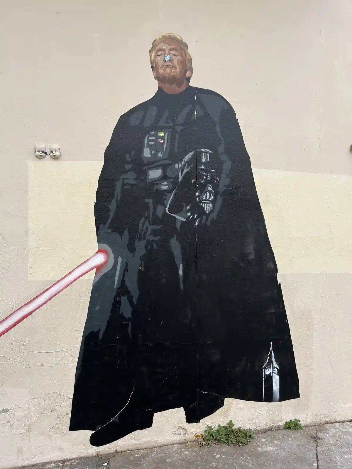 A street mural depicts a figure resembling Donald Trump dressed as Darth Vader, holding a red lightsaber, with a small clock…