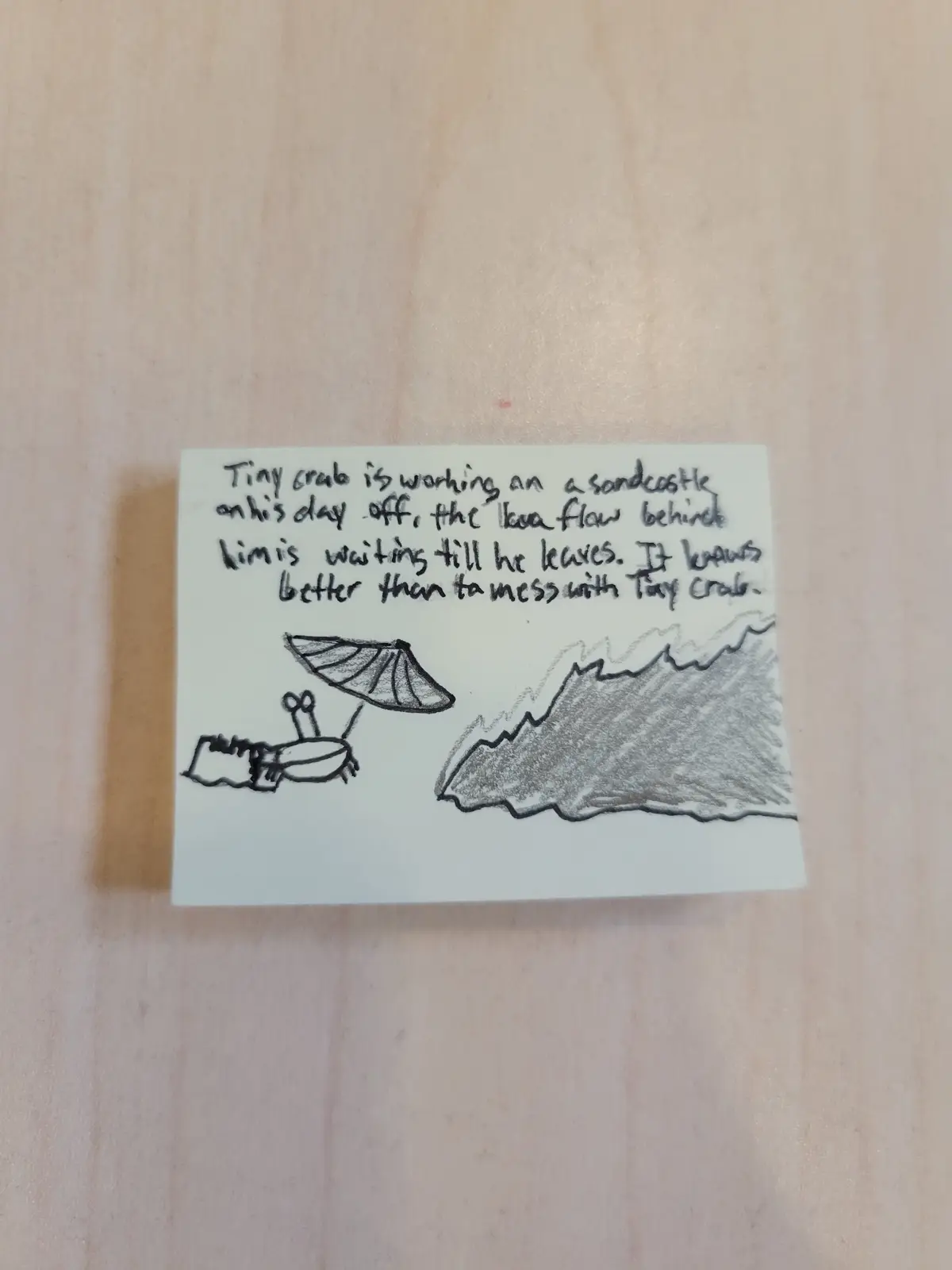 A hand-drawn sketch on a white sticky note shows a tiny crab relaxing under an umbrella next to a sandcastle, while a large…