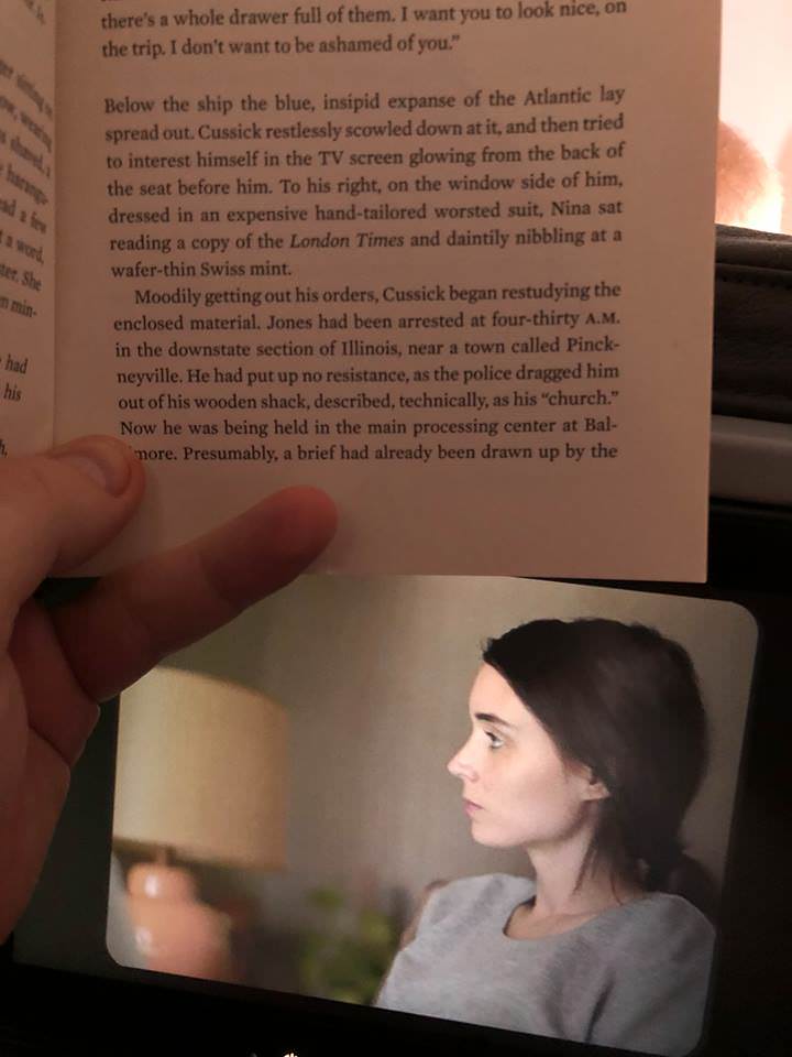 A person holds up a book open to a page of text, partially obscuring a photo of a woman with a pensive, tearful expression…