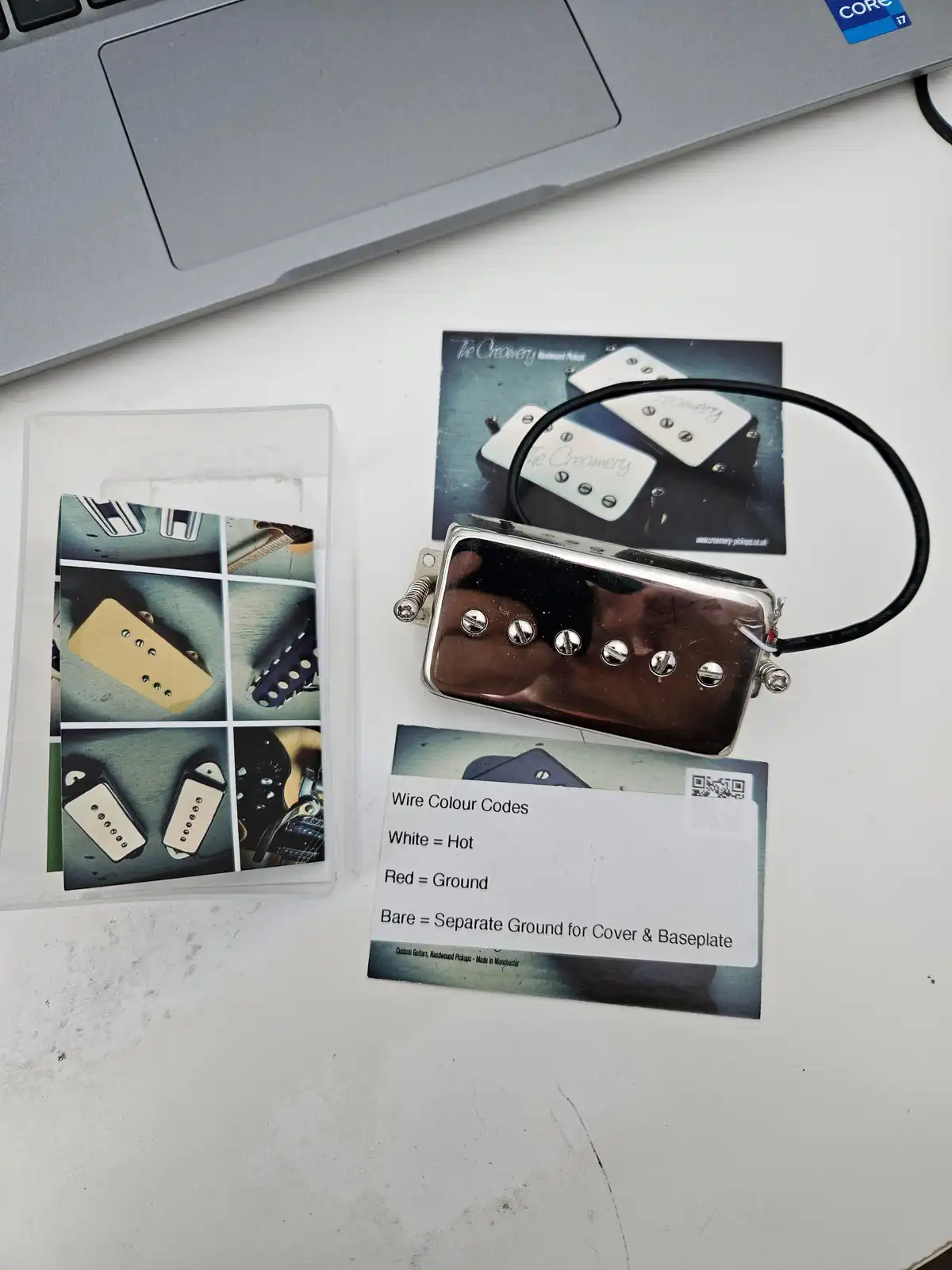A close-up photo shows a shiny chrome guitar pickup with a black wire attached, resting on a white surface next to a printed…