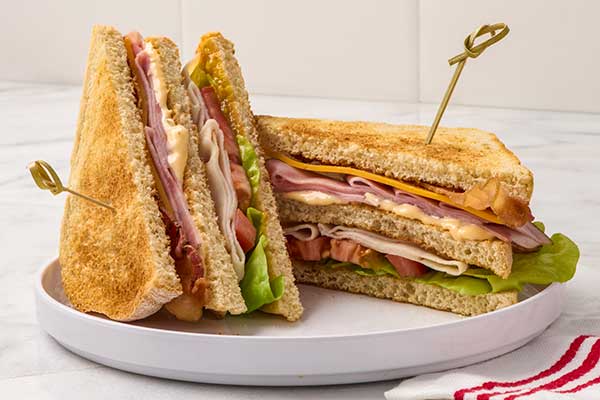 a club sandwich, cut diagonally into three triangular sections and held together with decorative toothpicks, is presented on…