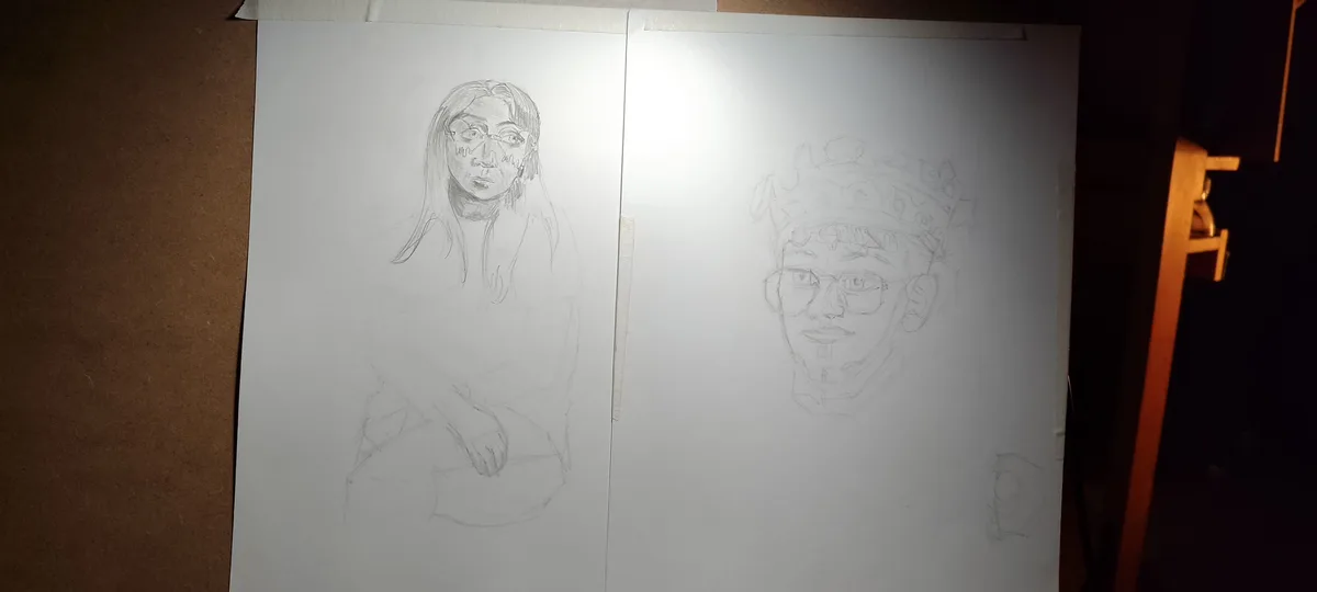 Two pencil sketches on separate white sheets taped side-by-side show a person with long hair and glasses on the left, and a…