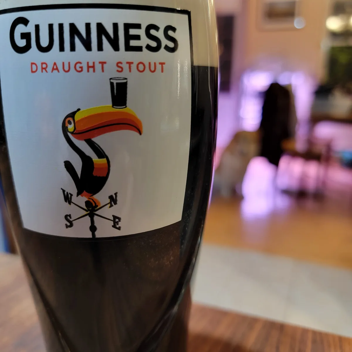 A close-up photo of a Guinness Draught Stout glass, showing its iconic label with a toucan perched on a weather vane, set…