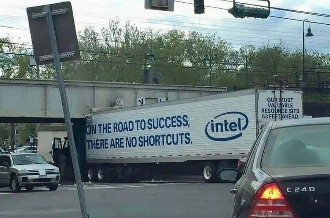 A white Intel-branded semi-truck is stuck under a low overpass, with its trailer visibly hitting the bridge. The truck's…
