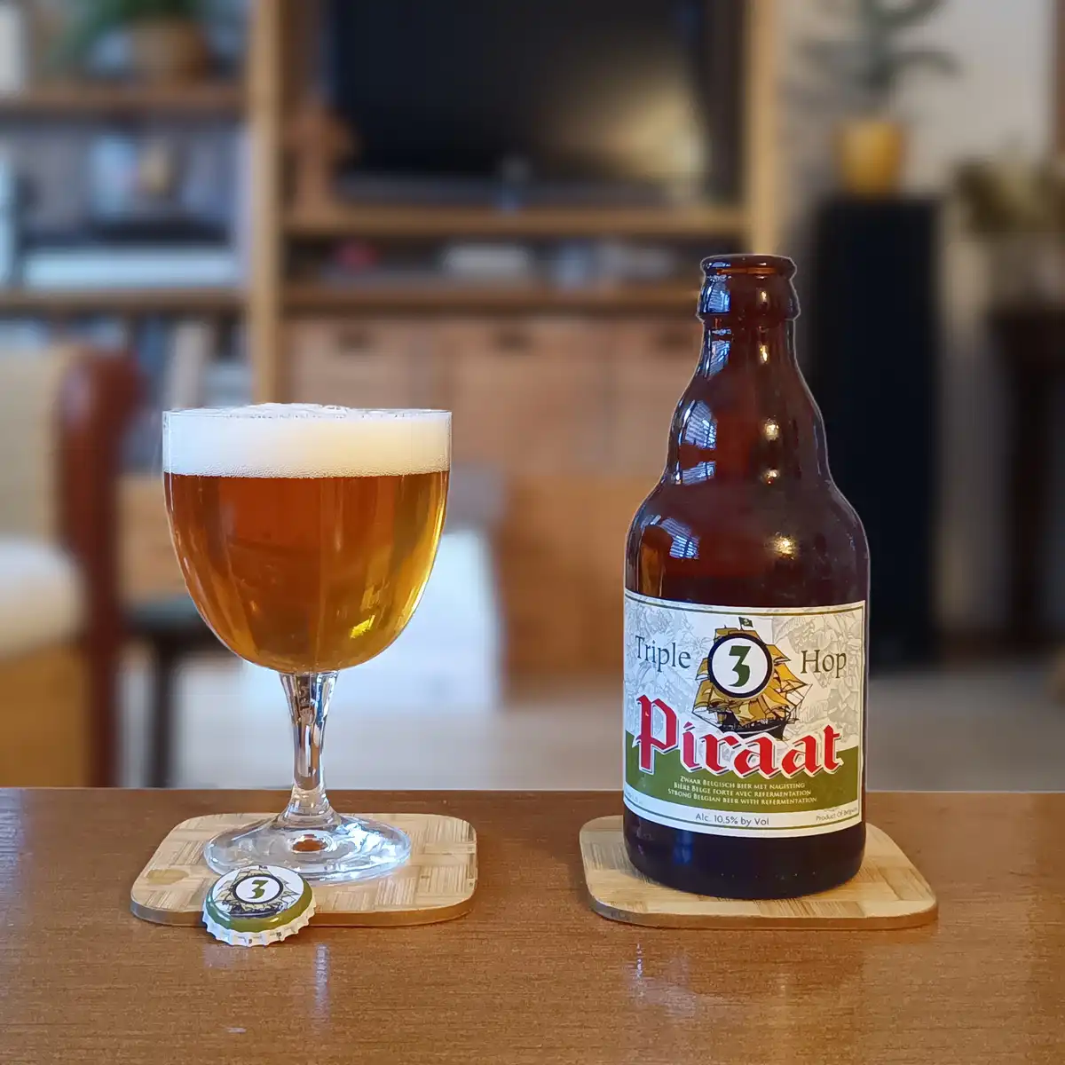A bottle of Triple 3 Hop Piraat Belgian beer sits next to a filled glass on wooden coasters, with the bottle cap beside the…
