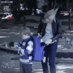 A woman and a young boy are at a playground. The woman, wearing a black jacket and sunglasses, initially holds the boy's…