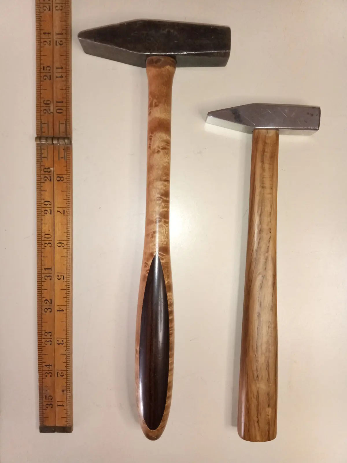Two wooden-handled hammers lie next to a wooden ruler showing measurements up to 35 inches. The larger hammer, with a dark…