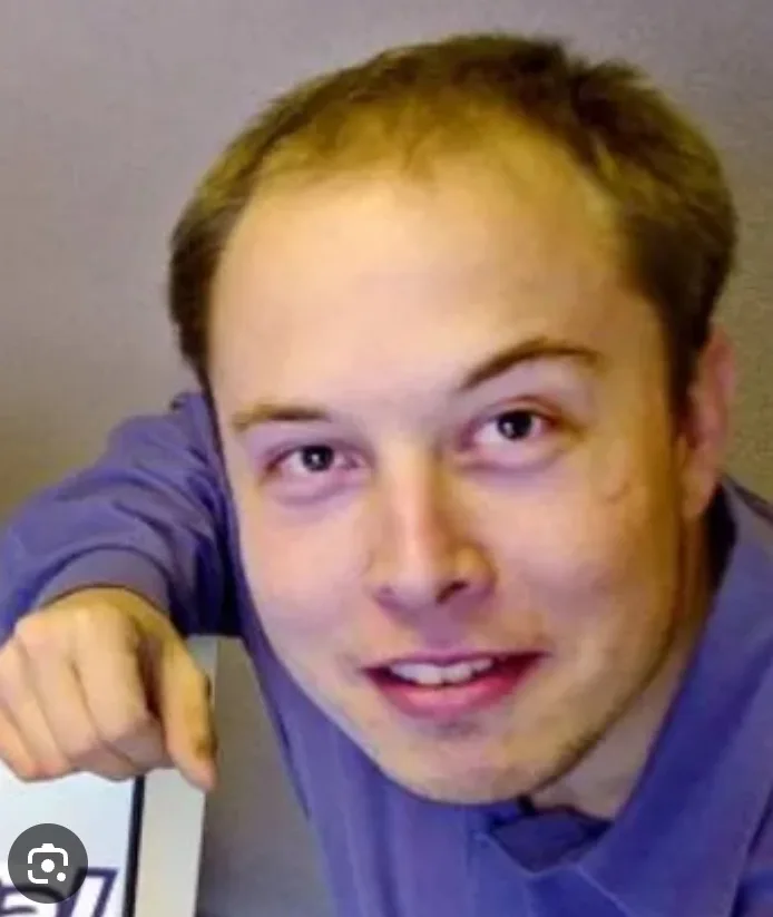 a close-up photo of a young man with thinning hair wearing a purple shirt, leaning forward with his right hand resting on a…