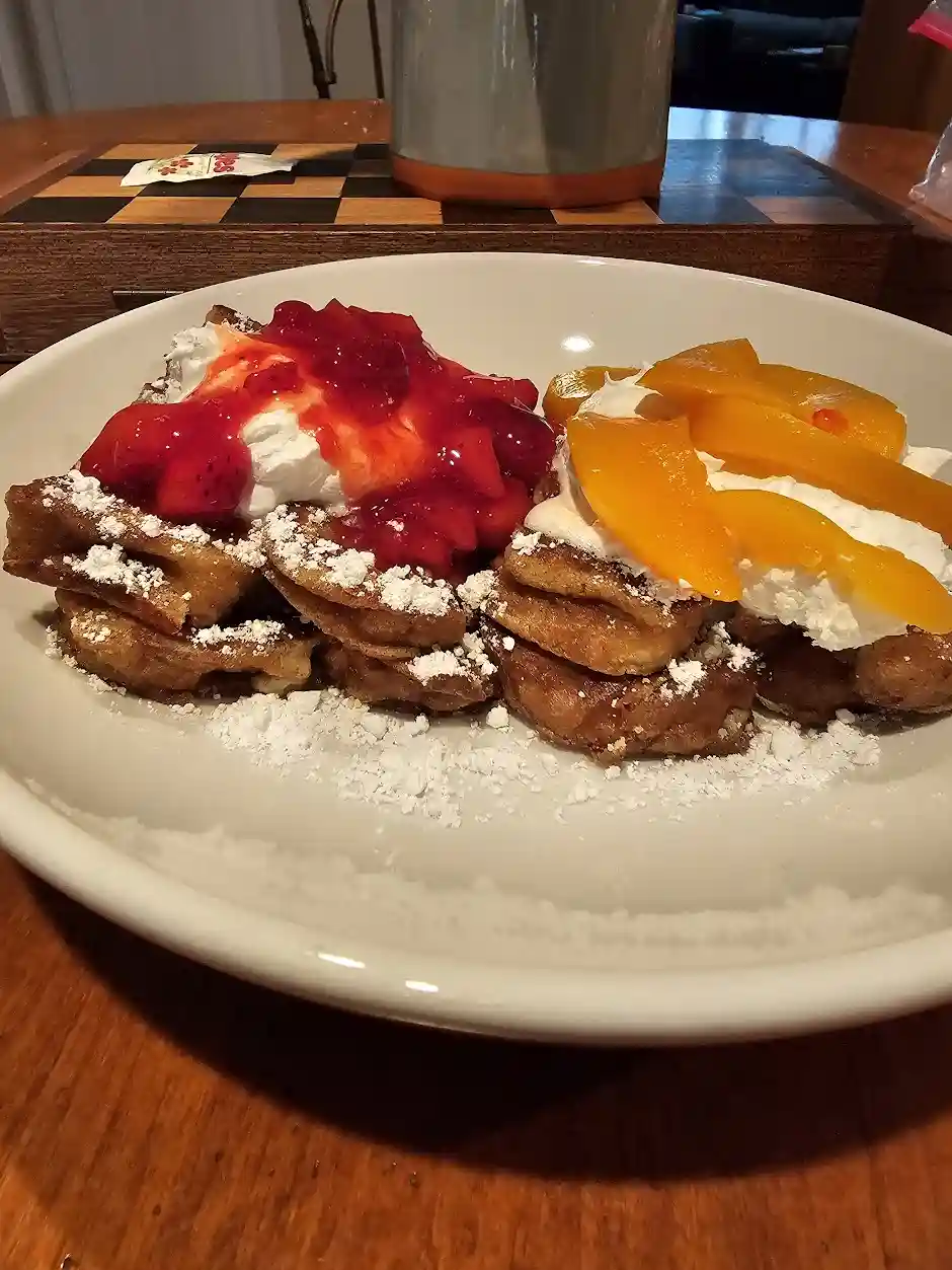 A close-up photo shows a white plate with two stacks of golden-brown french toast. The left stack is topped with whipped…