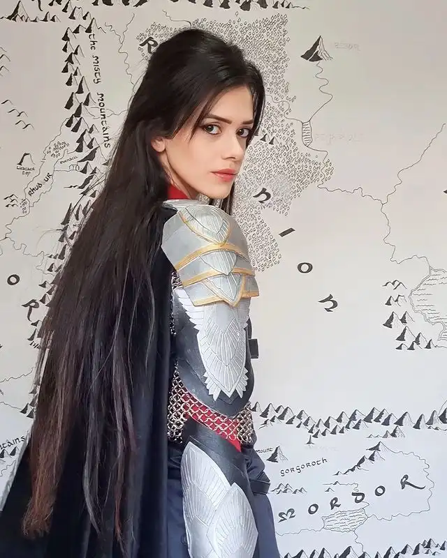 A woman in detailed silver and gold fantasy armor with a dark cape stands in profile, looking over her shoulder at the…