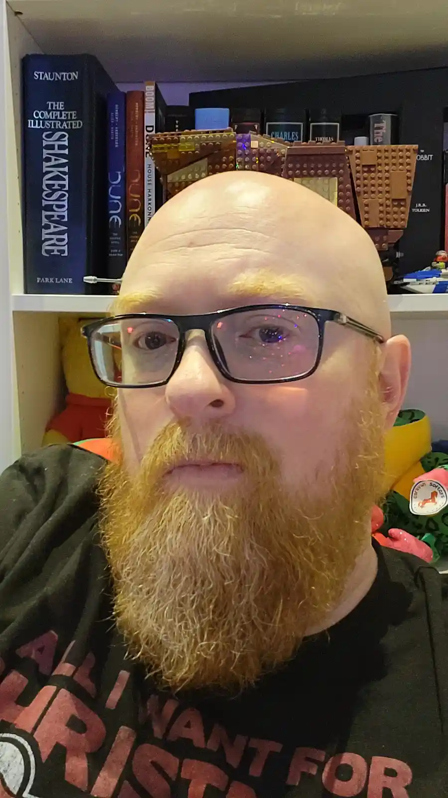 A bald man with a red beard and glasses stares directly at the camera, with a large, brown LEGO spaceship model placed on…